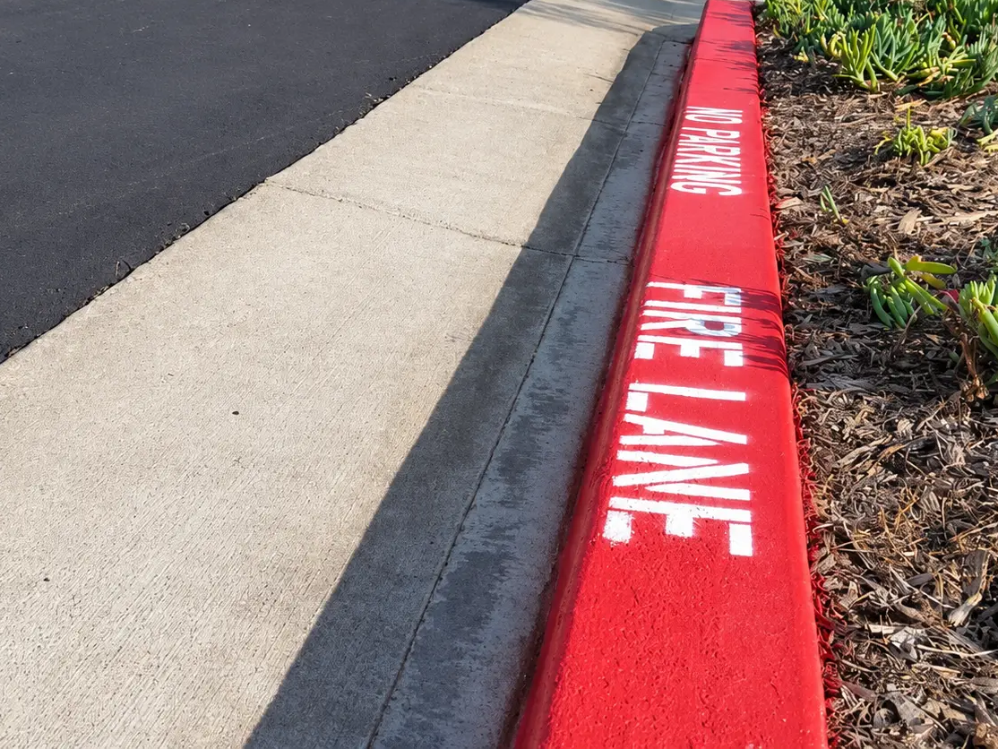 Red fire-lane curb with white FIRE LANE lettering painted along a commercial parking lot.